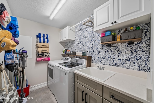 laundry room with cabinets, sink, light tile patterned floors, a textured ceiling, and washing machine and clothes dryer