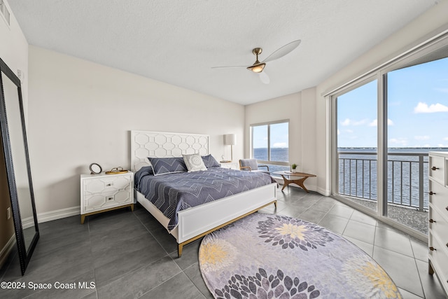 tiled bedroom featuring access to exterior, ceiling fan, a water view, and a textured ceiling