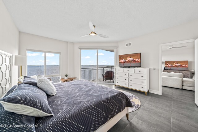 bedroom with ceiling fan, a water view, a textured ceiling, and access to outside