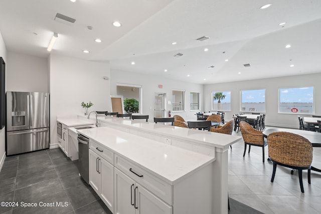 kitchen with light stone counters, stainless steel appliances, vaulted ceiling, sink, and white cabinets