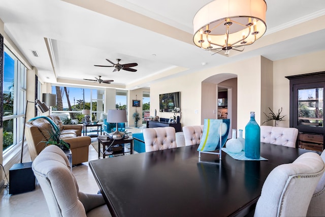 dining space with ceiling fan with notable chandelier, a tray ceiling, and plenty of natural light