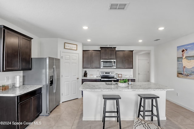 kitchen with appliances with stainless steel finishes, a kitchen bar, light tile patterned flooring, and a kitchen island with sink