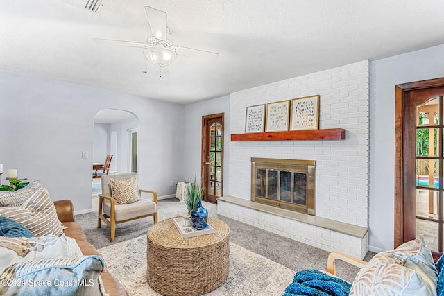 living room featuring light carpet, a textured ceiling, a fireplace, and ceiling fan