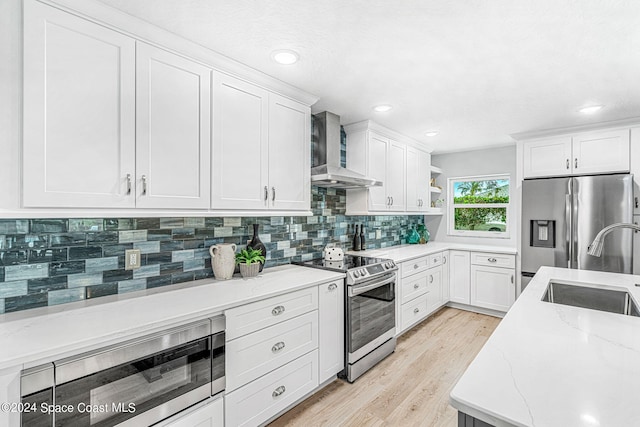 kitchen with white cabinetry, light stone countertops, light hardwood / wood-style flooring, wall chimney exhaust hood, and stainless steel appliances