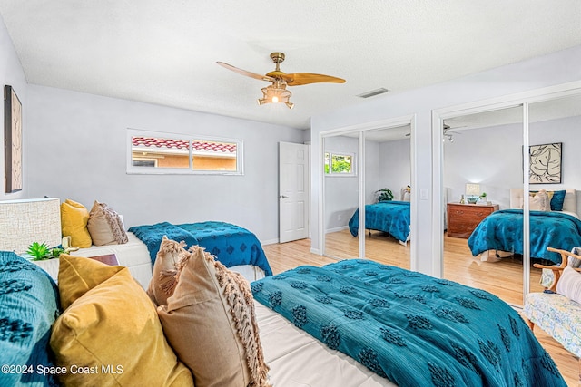 bedroom featuring ceiling fan, multiple closets, a textured ceiling, and light hardwood / wood-style floors