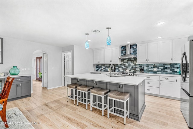 kitchen with wall chimney exhaust hood, sink, light wood-type flooring, white cabinets, and stainless steel refrigerator