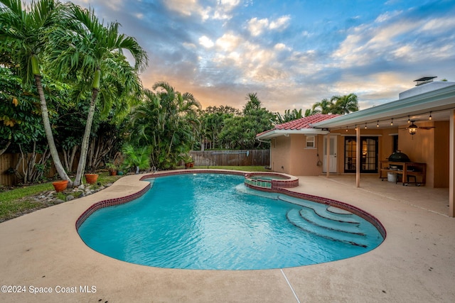 pool at dusk with an in ground hot tub, a patio, and ceiling fan