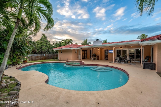 pool at dusk featuring a patio, an in ground hot tub, and ceiling fan