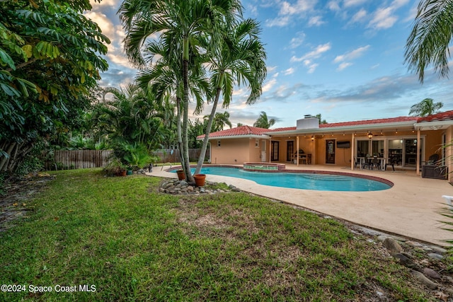 pool at dusk with an in ground hot tub, a yard, a patio, and ceiling fan