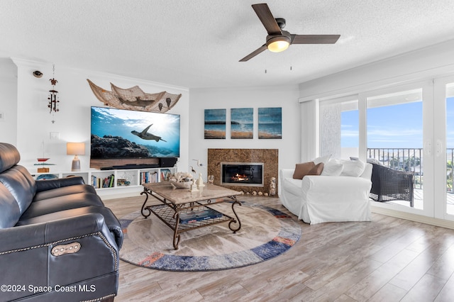 living room with wood-type flooring, a textured ceiling, ceiling fan, and a premium fireplace