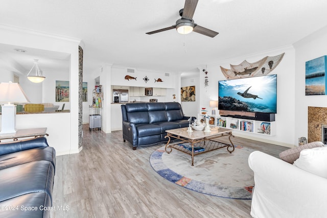 living room with a high end fireplace, light wood-type flooring, ceiling fan, and crown molding