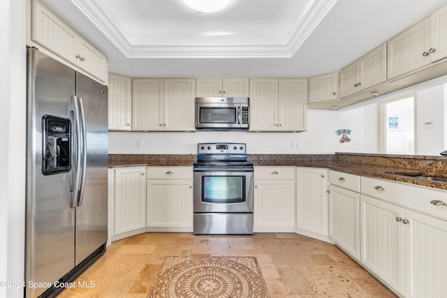 kitchen with appliances with stainless steel finishes, a tray ceiling, dark stone counters, and sink