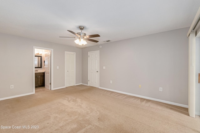 unfurnished bedroom featuring ensuite bathroom, light colored carpet, and ceiling fan