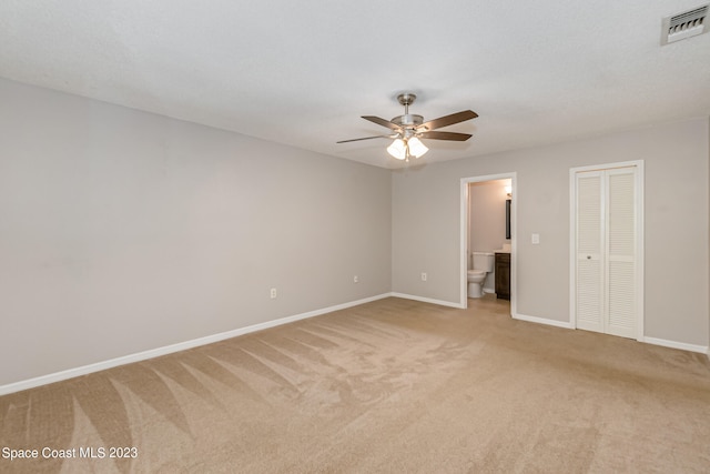 unfurnished bedroom with ensuite bathroom, light carpet, and ceiling fan