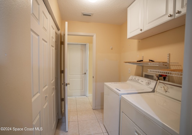 washroom with washer and clothes dryer, light tile patterned floors, cabinets, and a textured ceiling