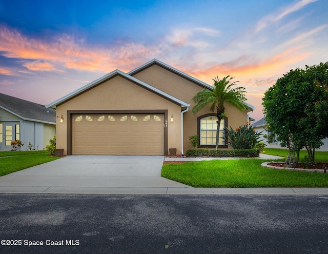 ranch-style home featuring driveway, a lawn, an attached garage, and stucco siding