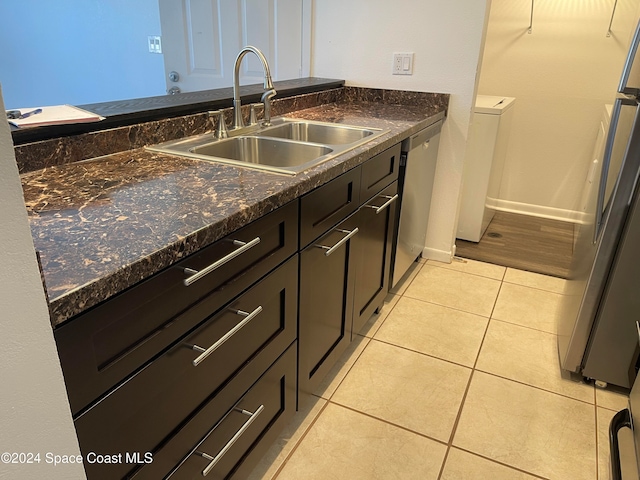 kitchen featuring washer / dryer, appliances with stainless steel finishes, sink, dark stone countertops, and light tile patterned floors