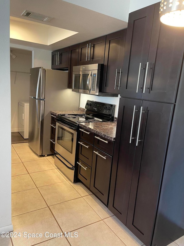 kitchen with washer / clothes dryer, stainless steel appliances, dark stone countertops, dark brown cabinetry, and light tile patterned floors