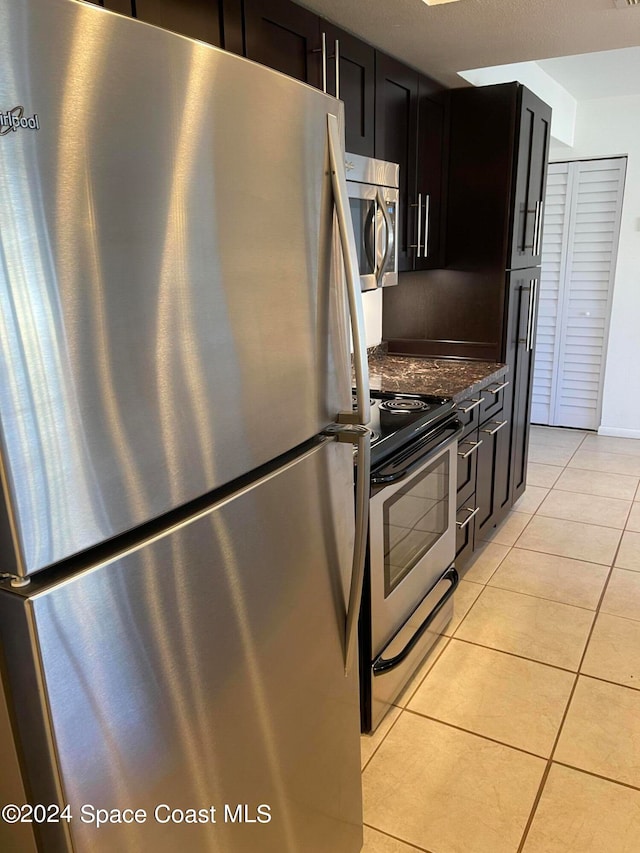 kitchen with appliances with stainless steel finishes, dark stone countertops, and light tile patterned flooring