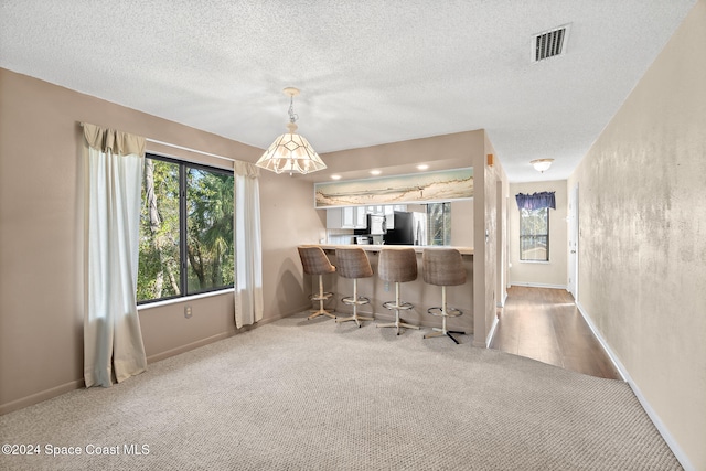 interior space featuring a textured ceiling, carpet floors, decorative light fixtures, and stainless steel fridge