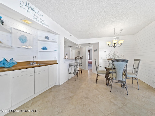 dining area featuring sink, a textured ceiling, an inviting chandelier, and wood walls