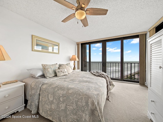 bedroom with access to exterior, carpet floors, a textured ceiling, a water view, and ceiling fan