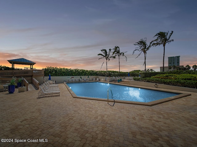 pool at dusk featuring a gazebo and a patio area