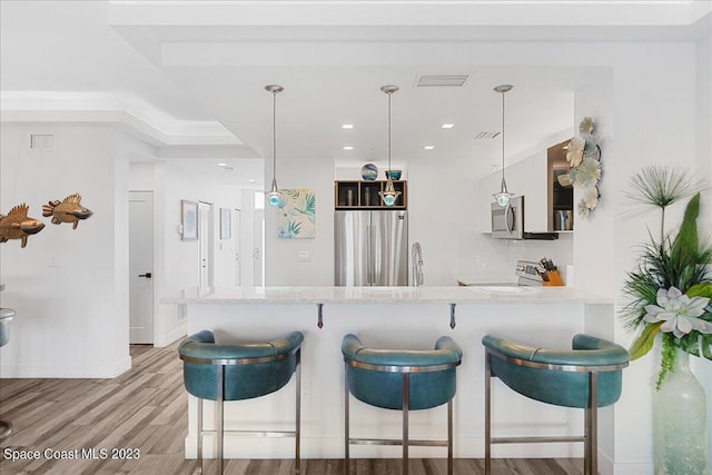 kitchen with kitchen peninsula, hanging light fixtures, backsplash, appliances with stainless steel finishes, and light hardwood / wood-style floors