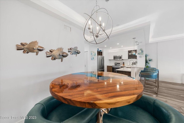 dining area with a chandelier, sink, light hardwood / wood-style floors, and a raised ceiling