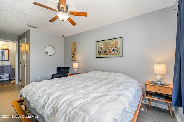 tiled bedroom with a textured ceiling, ceiling fan, and ensuite bath