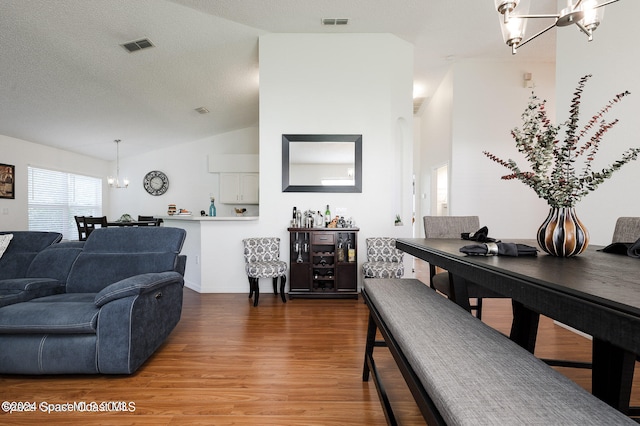 living room featuring a textured ceiling, vaulted ceiling, an inviting chandelier, and hardwood / wood-style floors