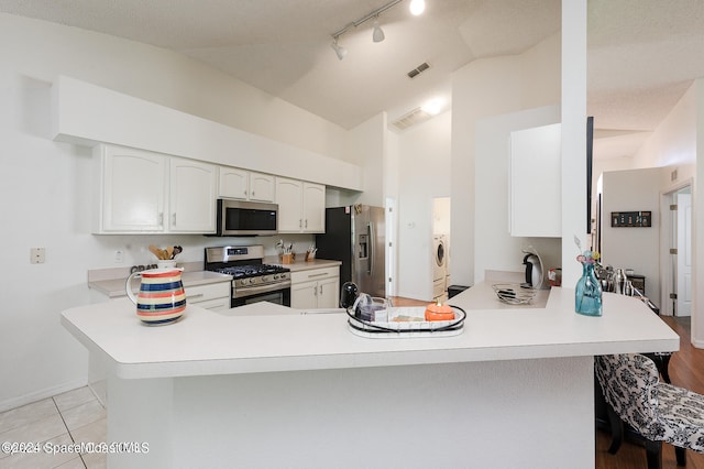 kitchen with kitchen peninsula, vaulted ceiling, white cabinetry, light tile patterned floors, and appliances with stainless steel finishes