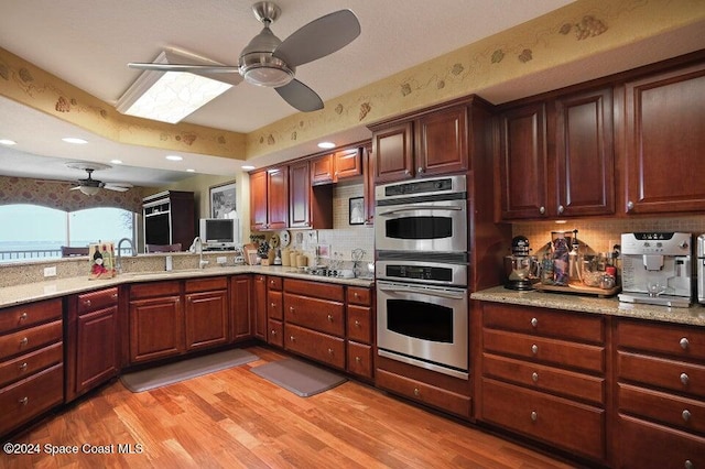 kitchen with stainless steel appliances, decorative backsplash, ceiling fan, light stone countertops, and light wood-type flooring