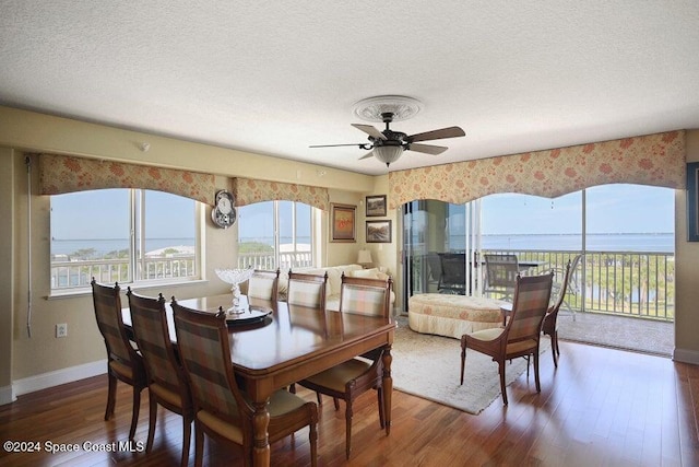 dining space with ceiling fan, a water view, a textured ceiling, and dark hardwood / wood-style floors