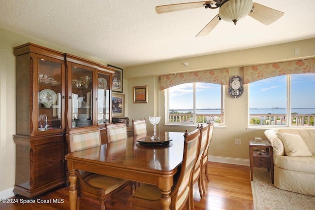 dining area featuring ceiling fan, wood-type flooring, a textured ceiling, and a water view