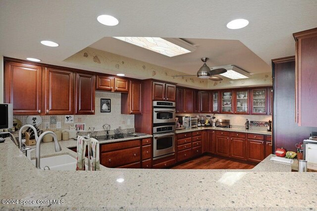 kitchen featuring sink, ceiling fan, a tray ceiling, stainless steel double oven, and dark wood-type flooring