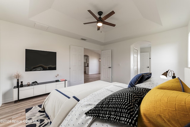 bedroom featuring ceiling fan, light wood-type flooring, and a raised ceiling