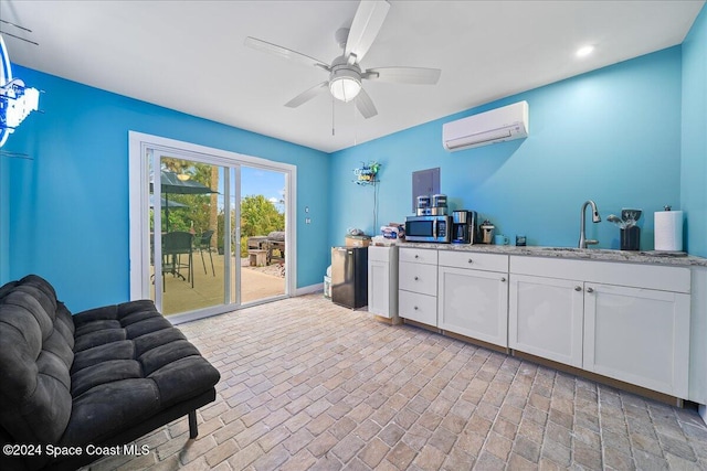 interior space with ceiling fan, a wall unit AC, sink, white cabinetry, and light stone countertops