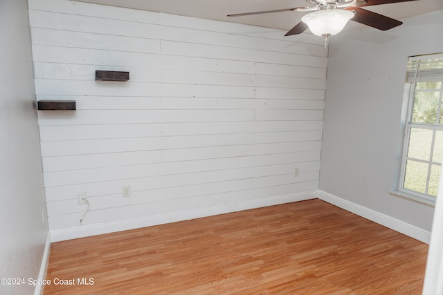 unfurnished room with ceiling fan, wood walls, and light hardwood / wood-style flooring