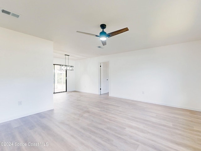 unfurnished room featuring ceiling fan with notable chandelier and light wood-type flooring