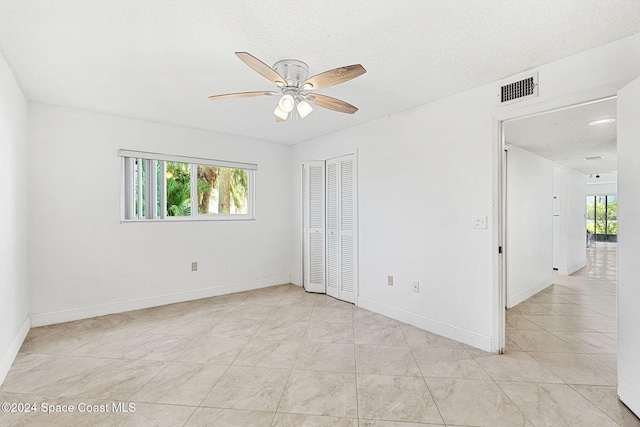 spare room with a textured ceiling, light tile patterned flooring, and ceiling fan