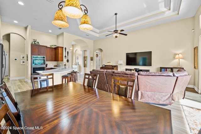 dining room featuring sink, a raised ceiling, ceiling fan, light hardwood / wood-style floors, and ornamental molding