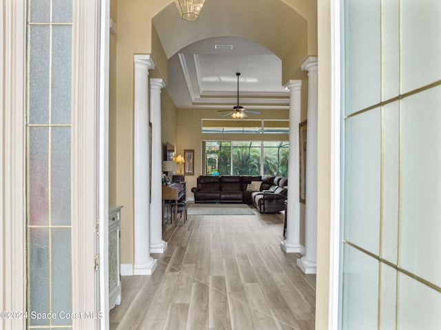 hall featuring ornate columns, crown molding, light wood-type flooring, and a raised ceiling