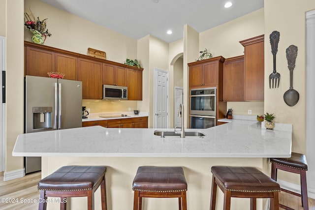 kitchen with appliances with stainless steel finishes, sink, light wood-type flooring, a kitchen bar, and kitchen peninsula