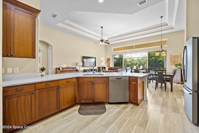 kitchen featuring kitchen peninsula, ceiling fan, appliances with stainless steel finishes, a tray ceiling, and light hardwood / wood-style floors