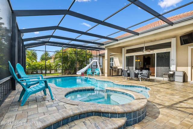 view of pool with glass enclosure, ceiling fan, a water slide, a patio area, and an in ground hot tub