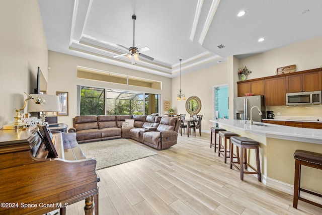 living room with ceiling fan, a raised ceiling, sink, and light wood-type flooring