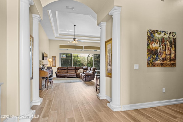 corridor featuring light hardwood / wood-style flooring, a tray ceiling, and decorative columns