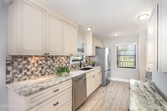 kitchen with light stone countertops, sink, stainless steel appliances, crown molding, and cream cabinetry