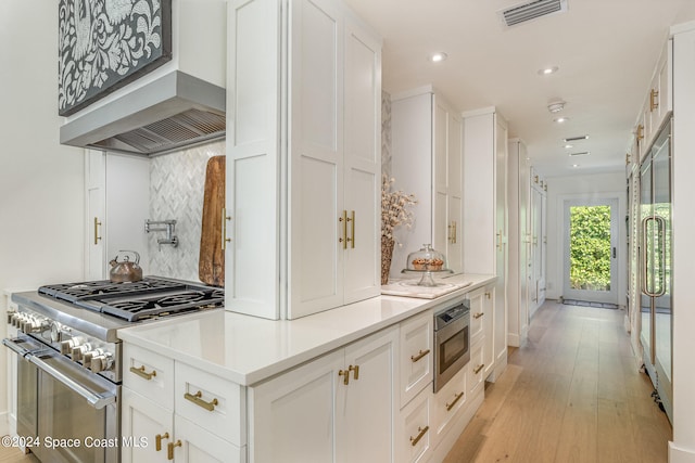 kitchen with high end stove, oven, white cabinetry, and wall chimney range hood